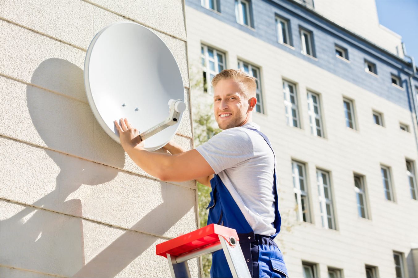 Ein Mann bringt eine Satellitenschüssel an eine Hauswand
